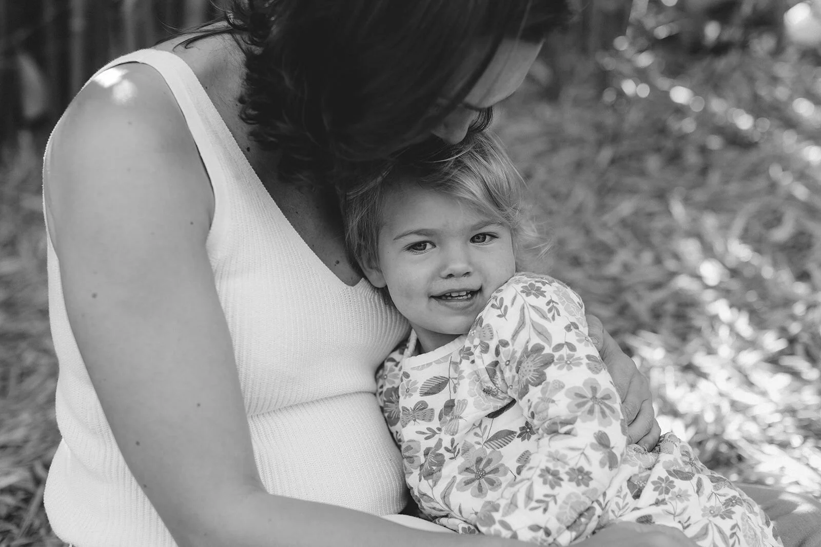 Black and white close-up of a toddler smiling in her mum's arms
