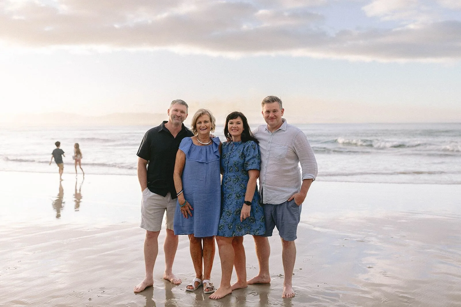 Two couples, the parents and grandparents, standing together on the beach at sunset