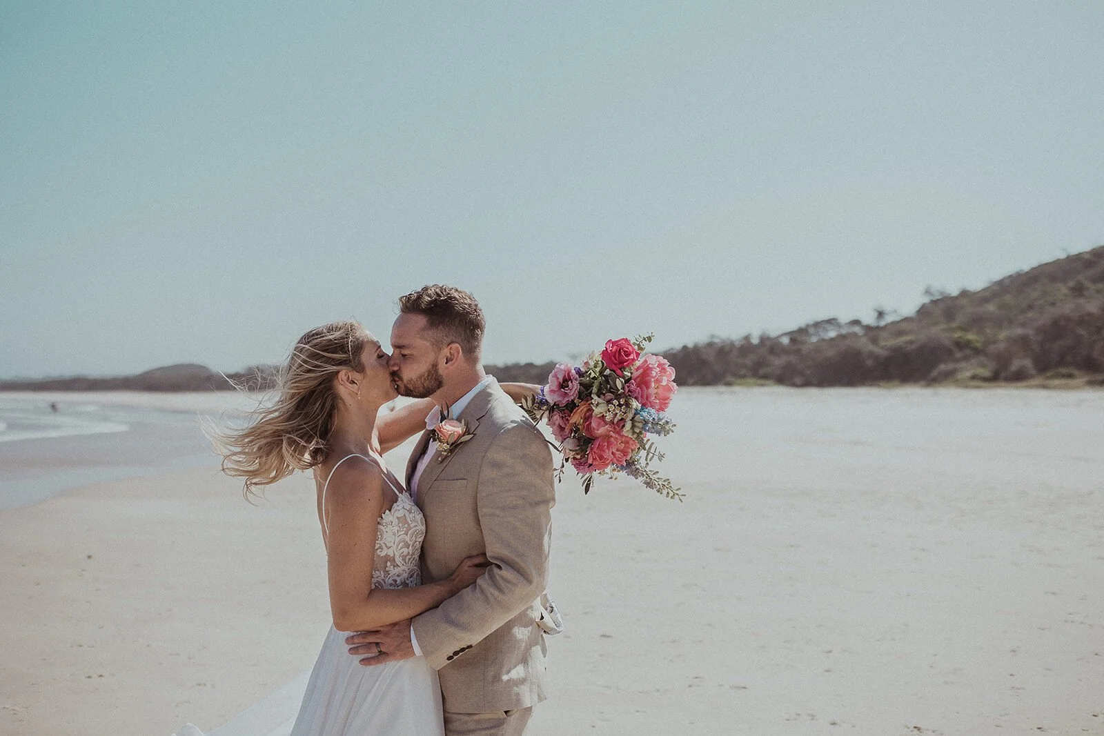 Couple kissing on the beach with the bouquet, Eliza and Greg's elopement at Broken Head, Byron Bay