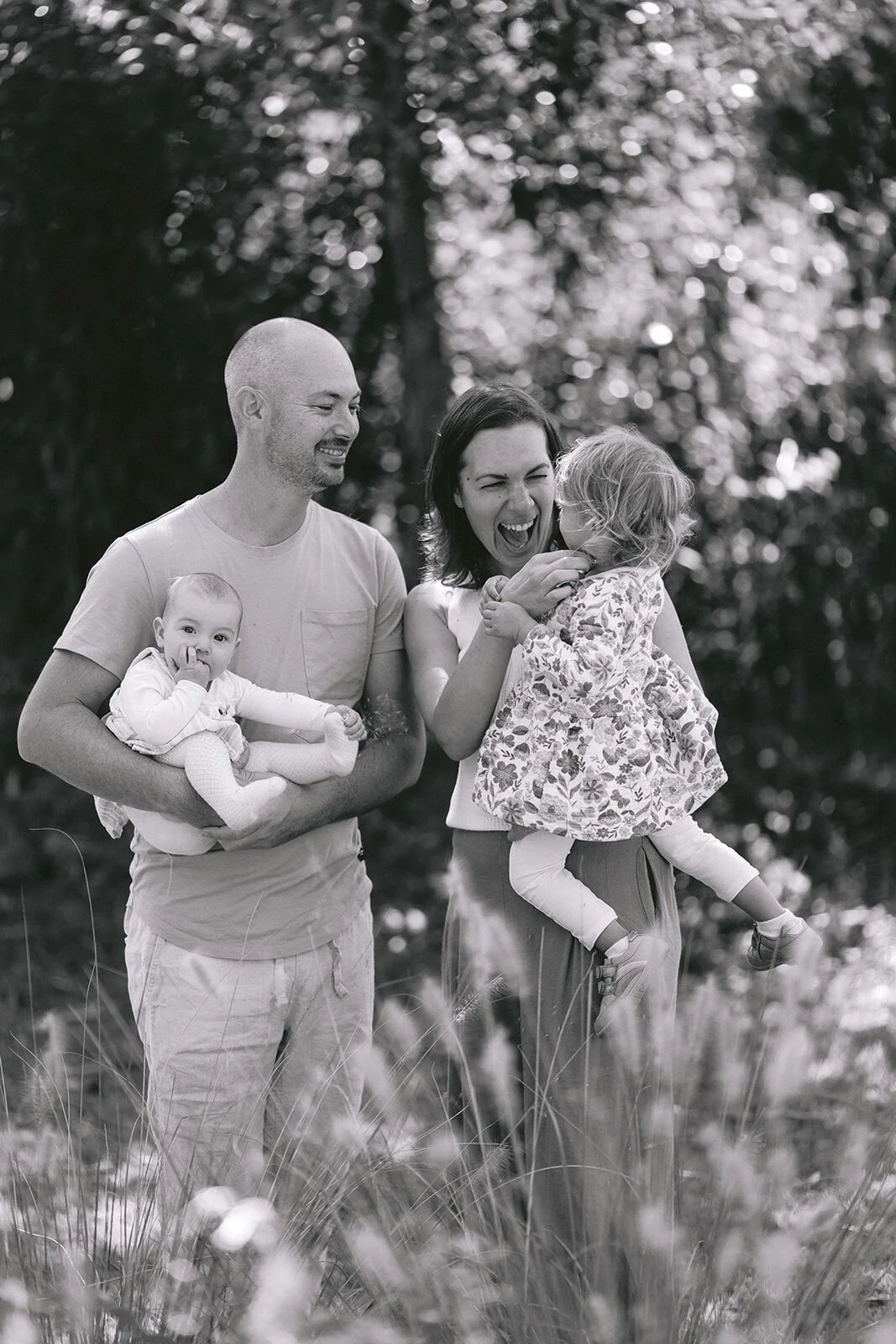 Black and white photo of parents laughing with their two girls in a field of grasses