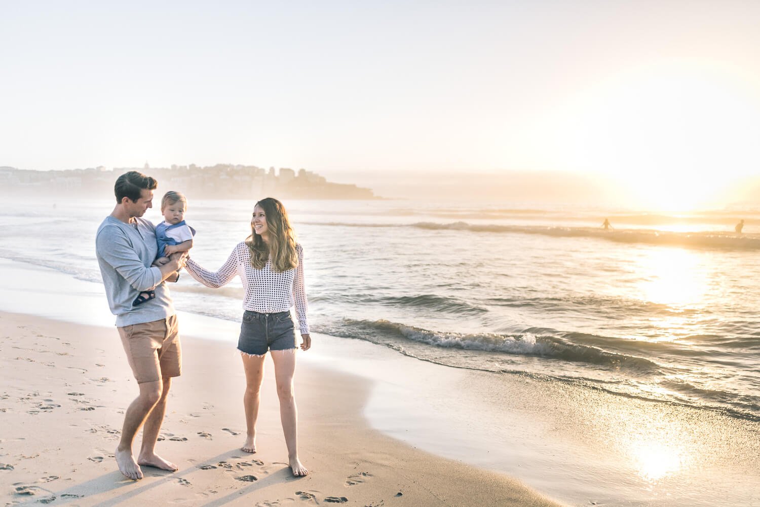 Parents walking along the shoreline at Bondi at sunrise with their little boy