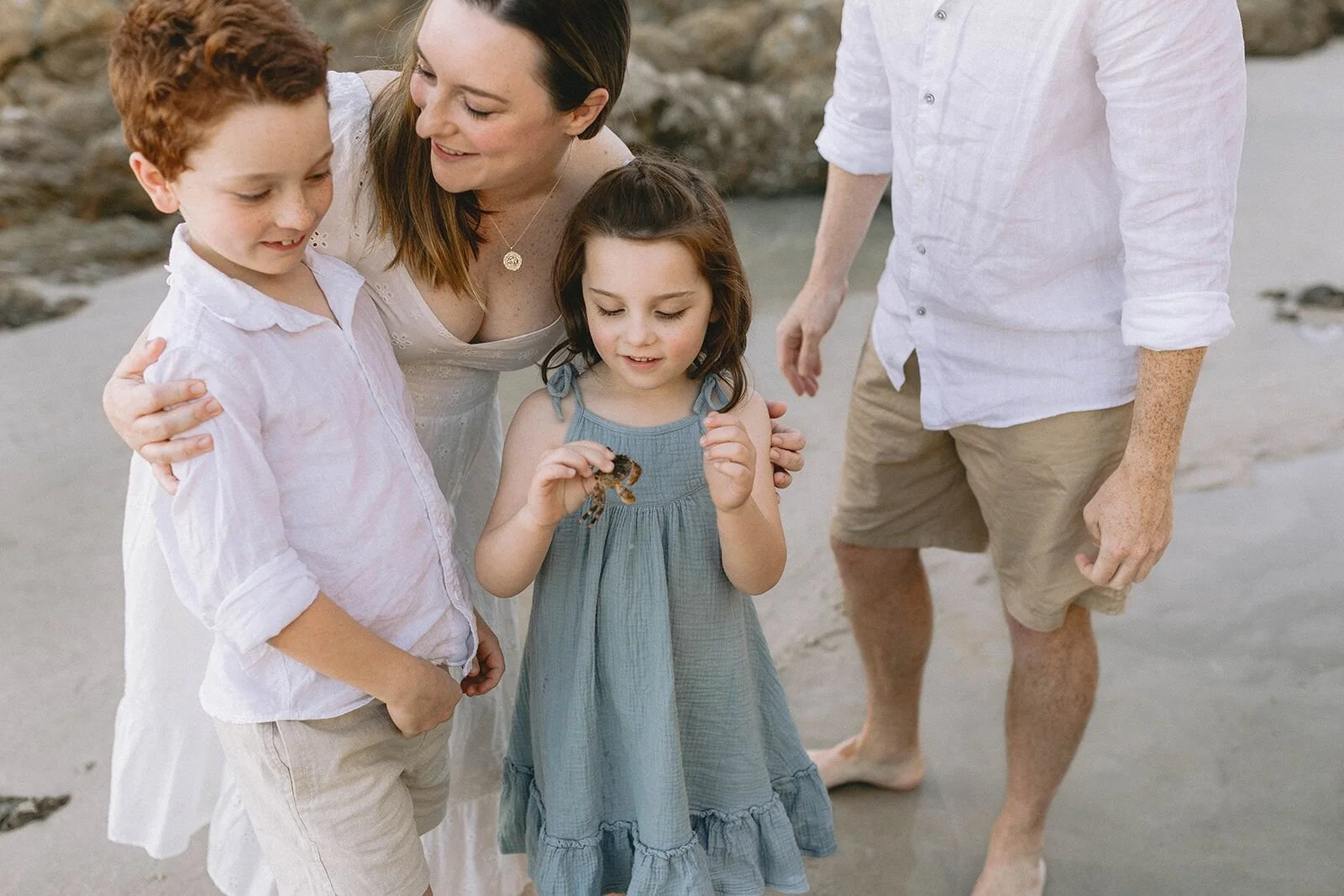 Little girl in a sage green dress holding a tiny shell, with her brother, mum and dad beside her