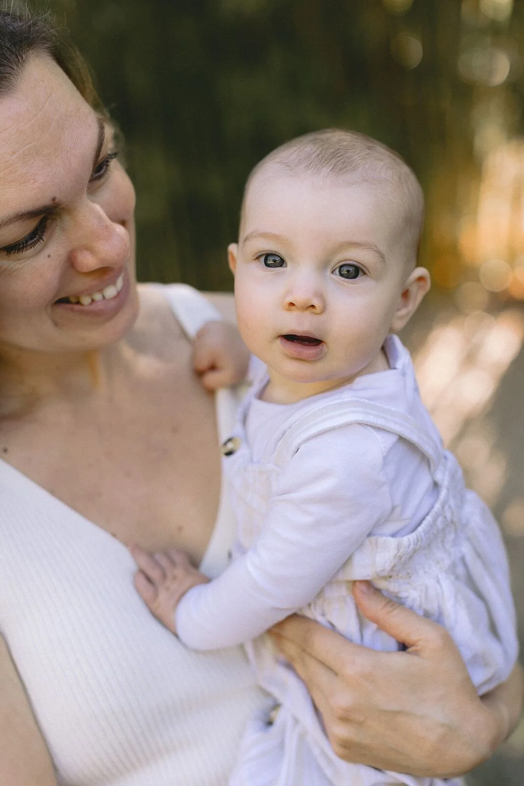 Mum smiling down at her baby, who looks straight to camera, bamboo grove background