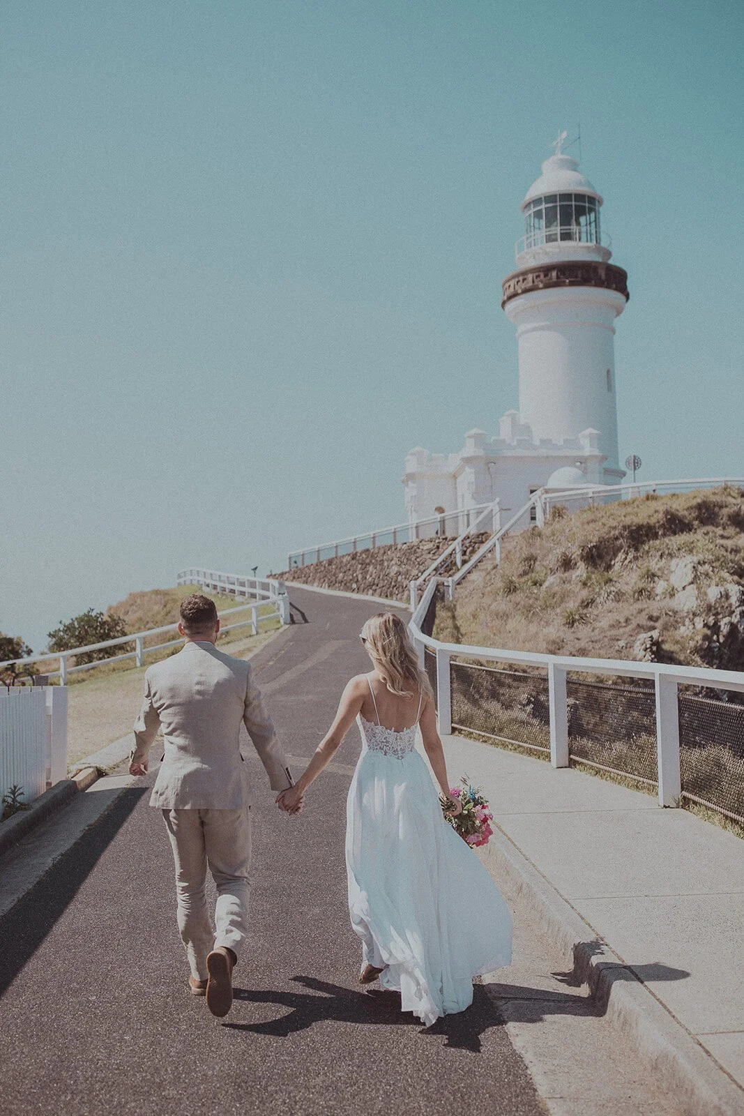 Couple walking hand in hand toward Cape Byron Lighthouse, Eliza and Greg's elopement at Broken Head, Byron Bay