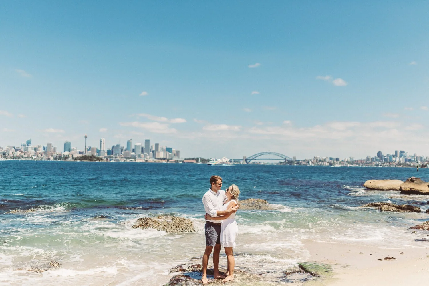 Couple embracing on the Shark Island rock shelf with the Harbour Bridge and city behind