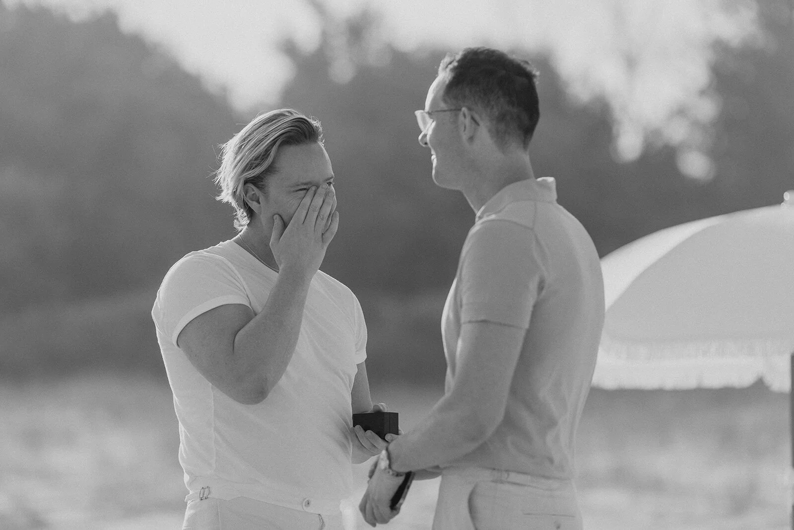 Black and white of a man covering his face with emotion as he holds the ring box, Byron and Luke's marriage proposal at Cabarita Beach, Northern Rivers