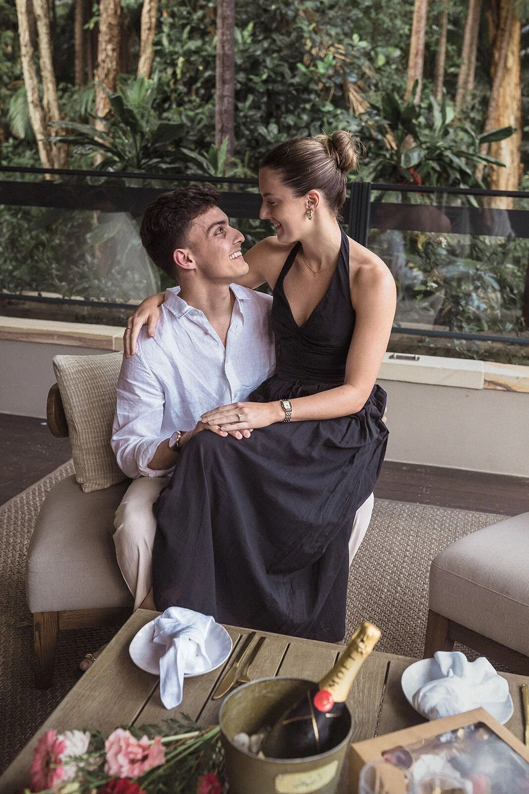 Woman smiling at her fiancé from his lap on the lounge, Ben and Chloe's marriage proposal in Byron Bay