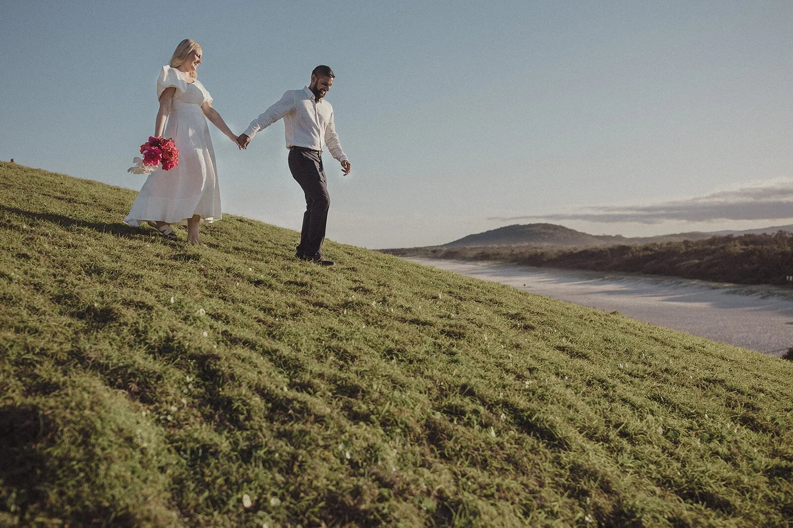 Couple walking hand in hand down the grassy slope, Brittany and Mark's elopement at Cabarita Beach, Northern Rivers