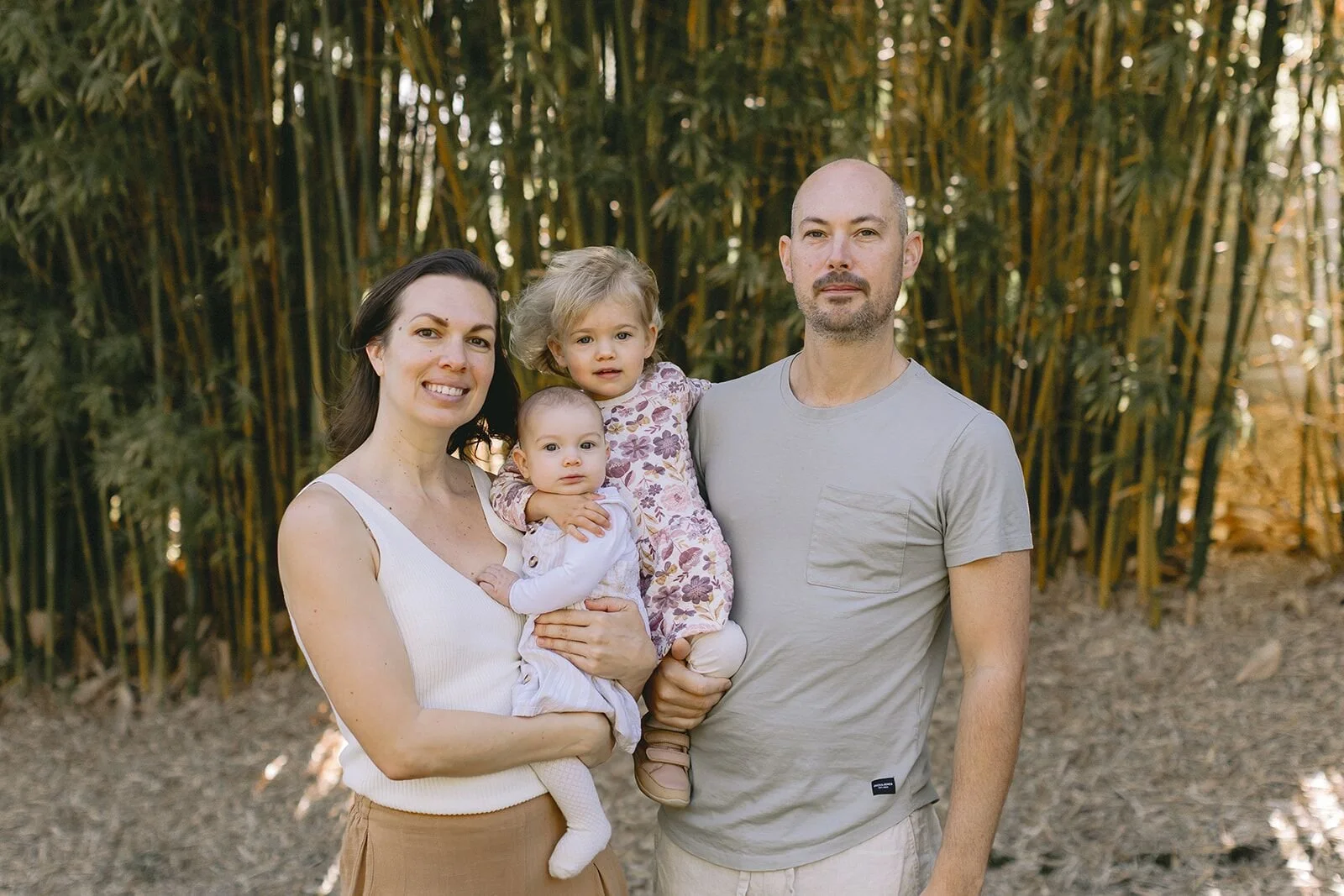 Family portrait of mum, dad and two little girls standing together in front of golden bamboo