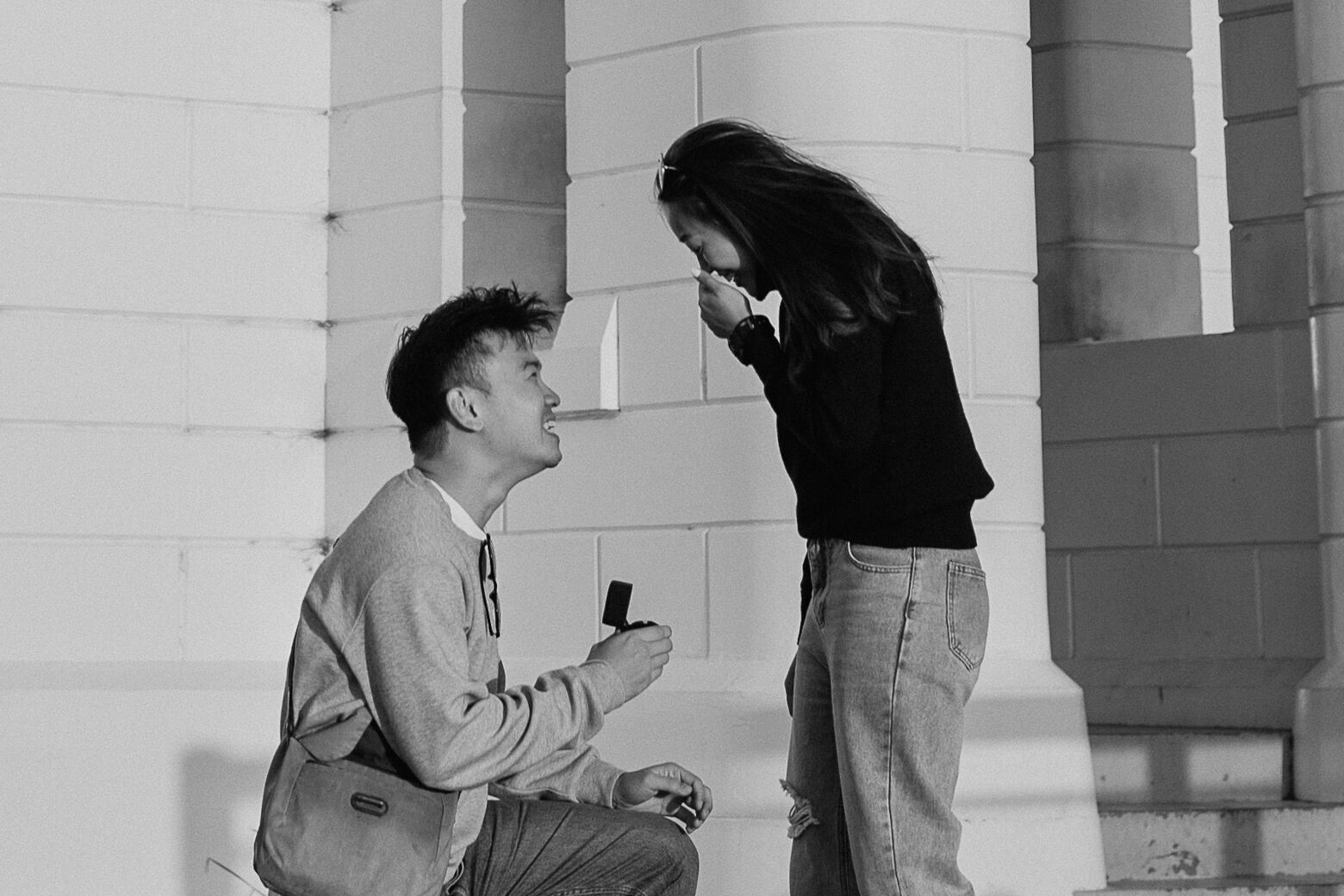Black and white close up of the man kneeling with the ring box as the woman covers her mouth, Douglas and Ying's sunset marriage proposal at Cape Byron Lighthouse, Byron Bay