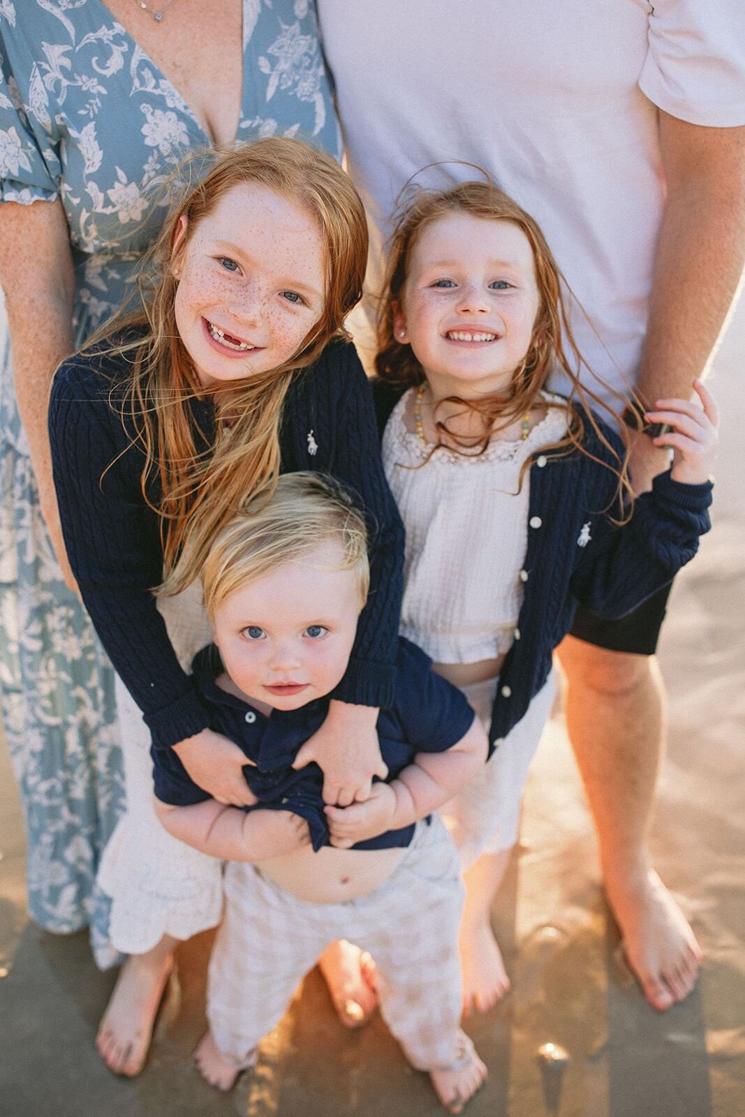 Two sisters and their toddler brother smiling at the camera, held close by their parents