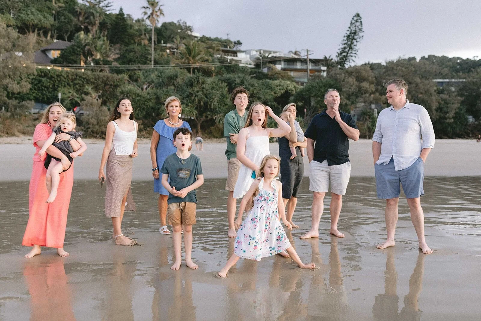 Whole family standing on the beach, children playing and adults laughing, Byron Bay in the background