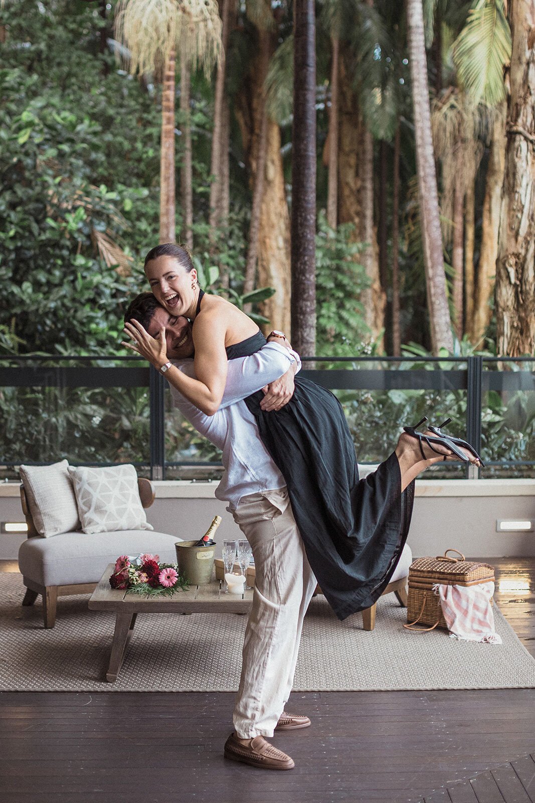 Man lifting his fiancée off the ground, both laughing, Ben and Chloe's marriage proposal in Byron Bay