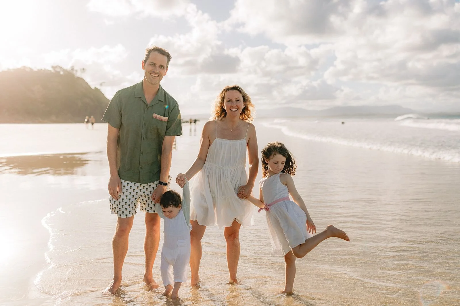 Family paddling in the shallows at Wategos, the daughter kicking up her leg and laughing