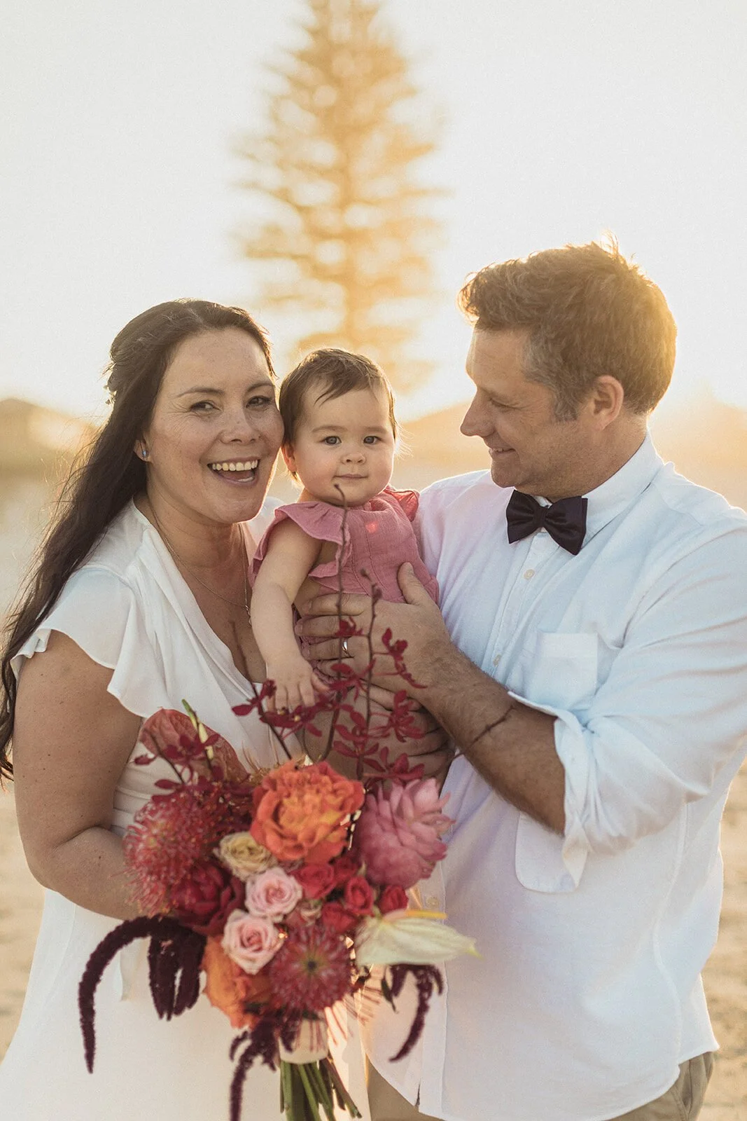 Couple laughing with the baby and bouquet, Maritess and Mark's elopement at Lennox Head