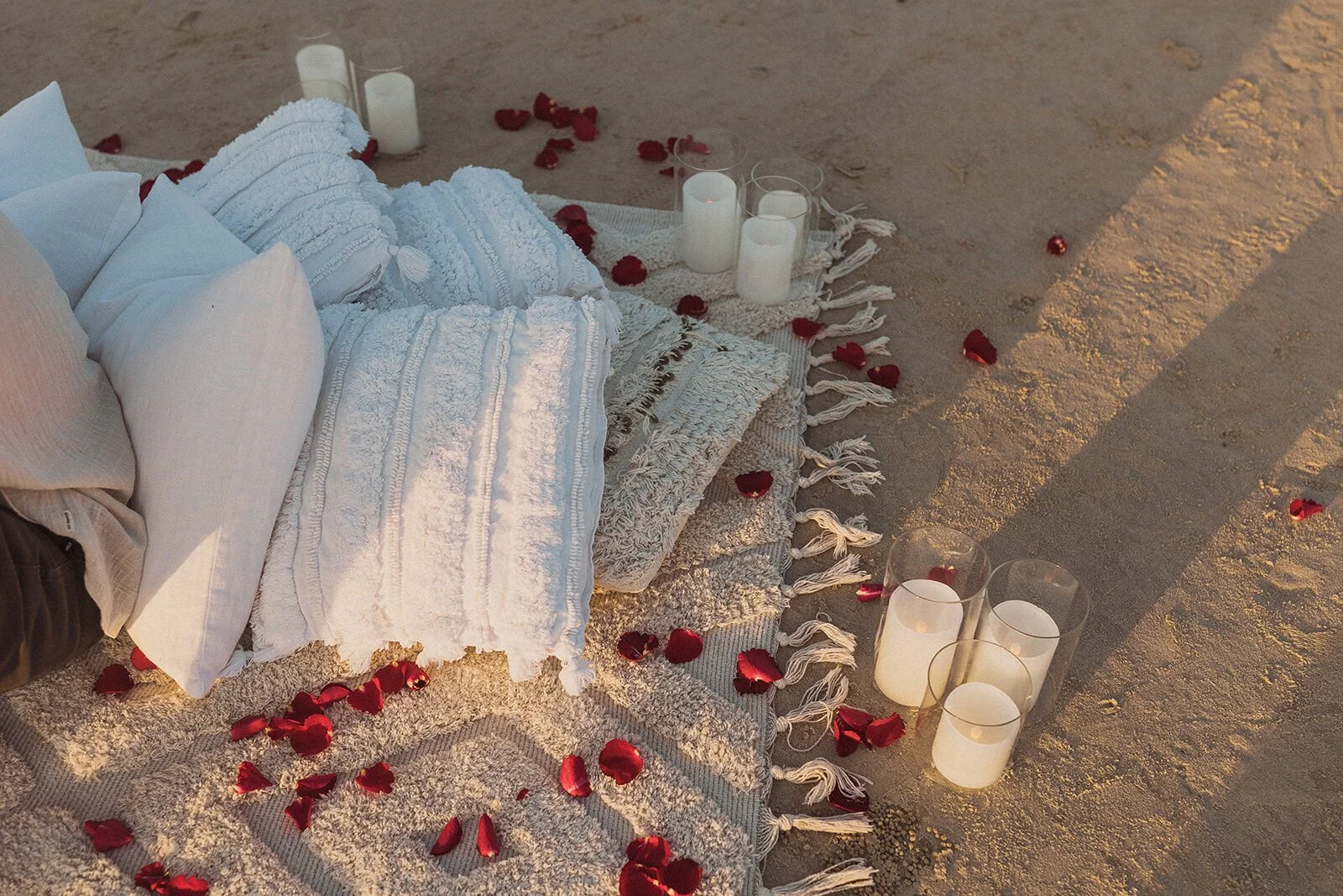 Detail of pillows, rug, rose petals and candles set up on the sand, Charlie and Hannah's sunrise marriage proposal at Broken Head Beach, Byron Bay
