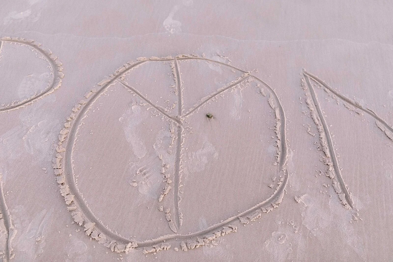 A peace symbol and lettering drawn in the sand on the beach