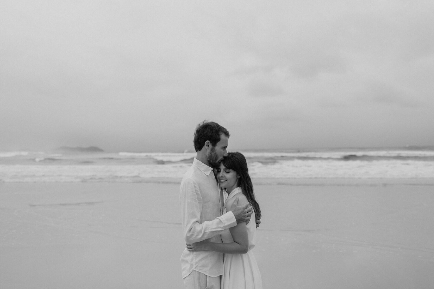 Black and white of the couple embracing at the shoreline, Yoanne and Elisa's rainy elopement at Broken Head, Byron Bay