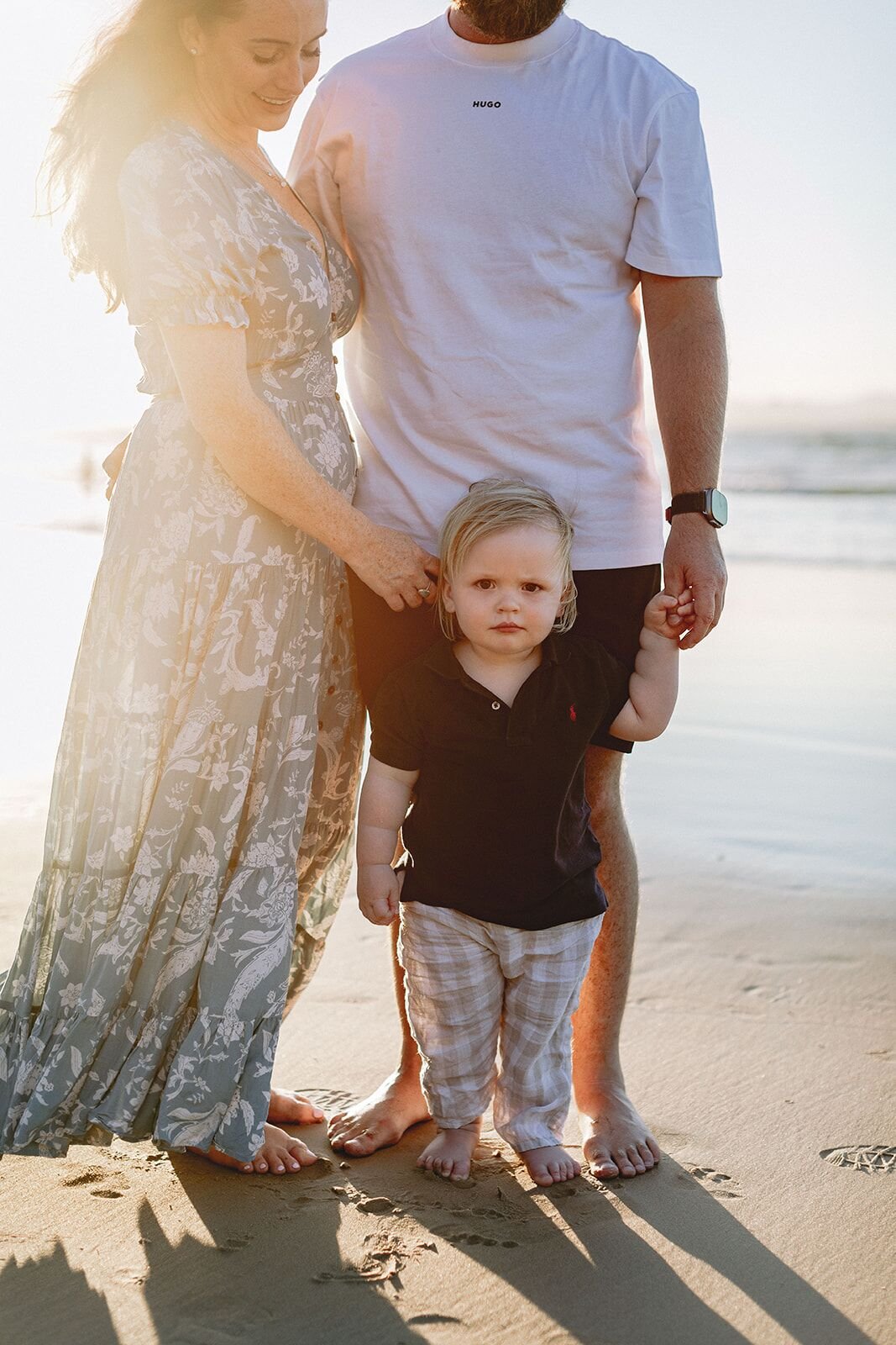 Toddler standing between his parents on the sand in warm low sun