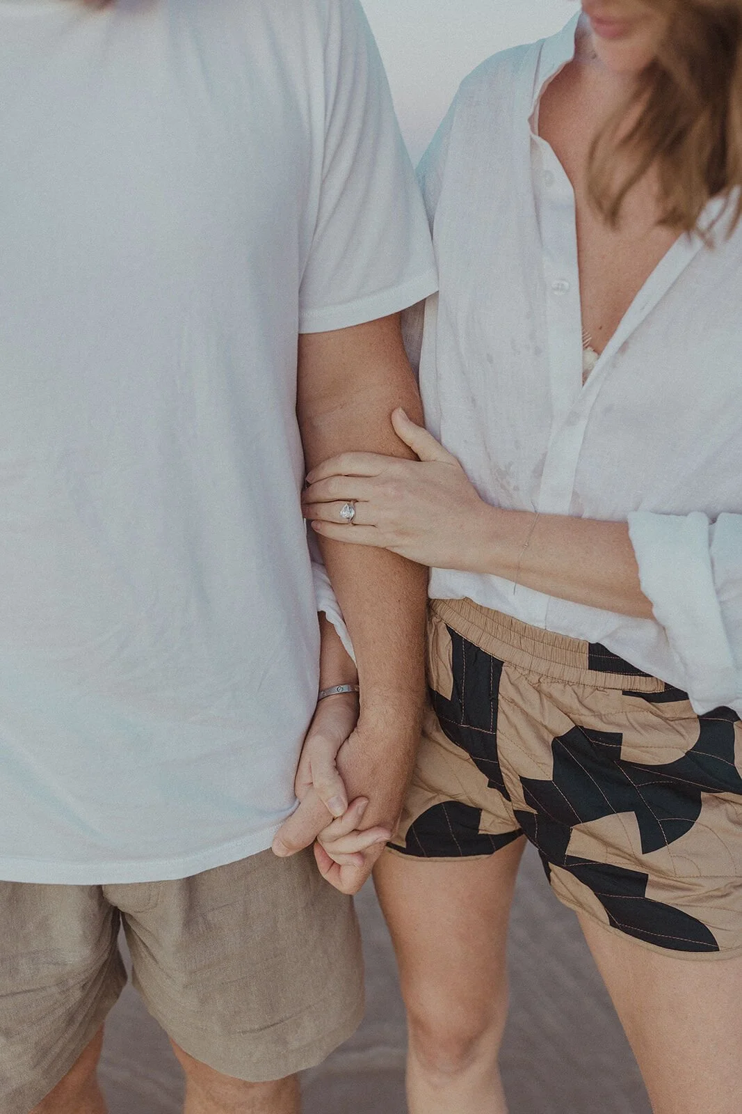 Close up of the couple holding hands, her engagement ring on his arm, Jamie and Jessica's beach marriage proposal at Belongil Beach, Byron Bay