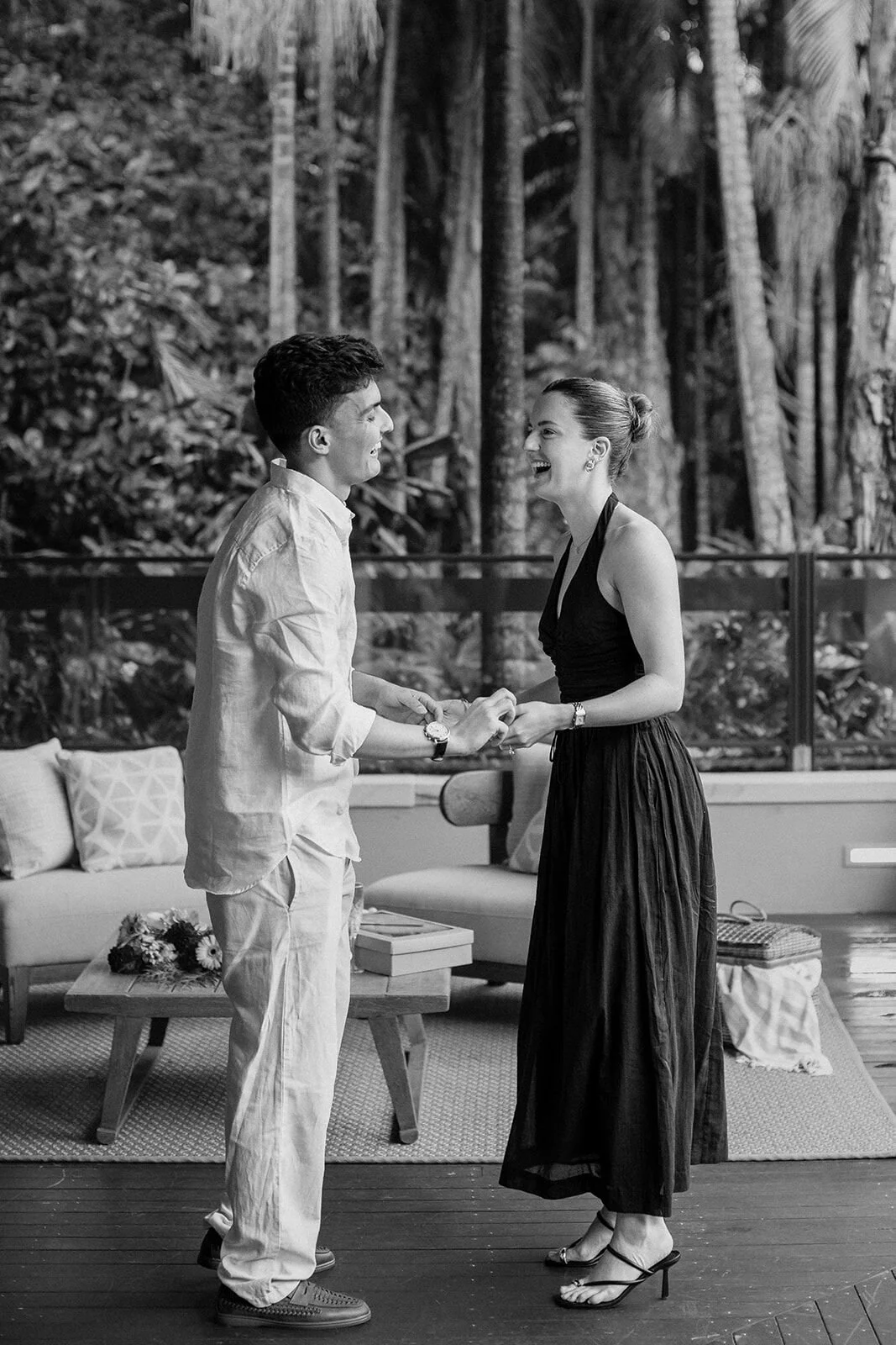 Black and white of the couple laughing and holding hands on the deck, Ben and Chloe's marriage proposal in Byron Bay