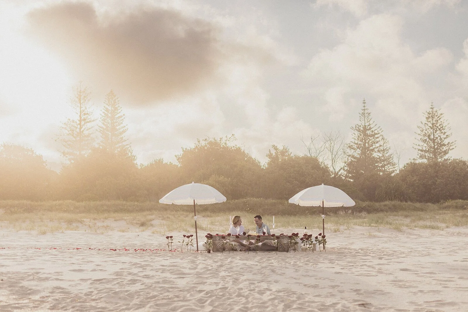 Couple small in the distance at their beach picnic in warm sunset light, Byron and Luke's marriage proposal at Cabarita Beach, Northern Rivers