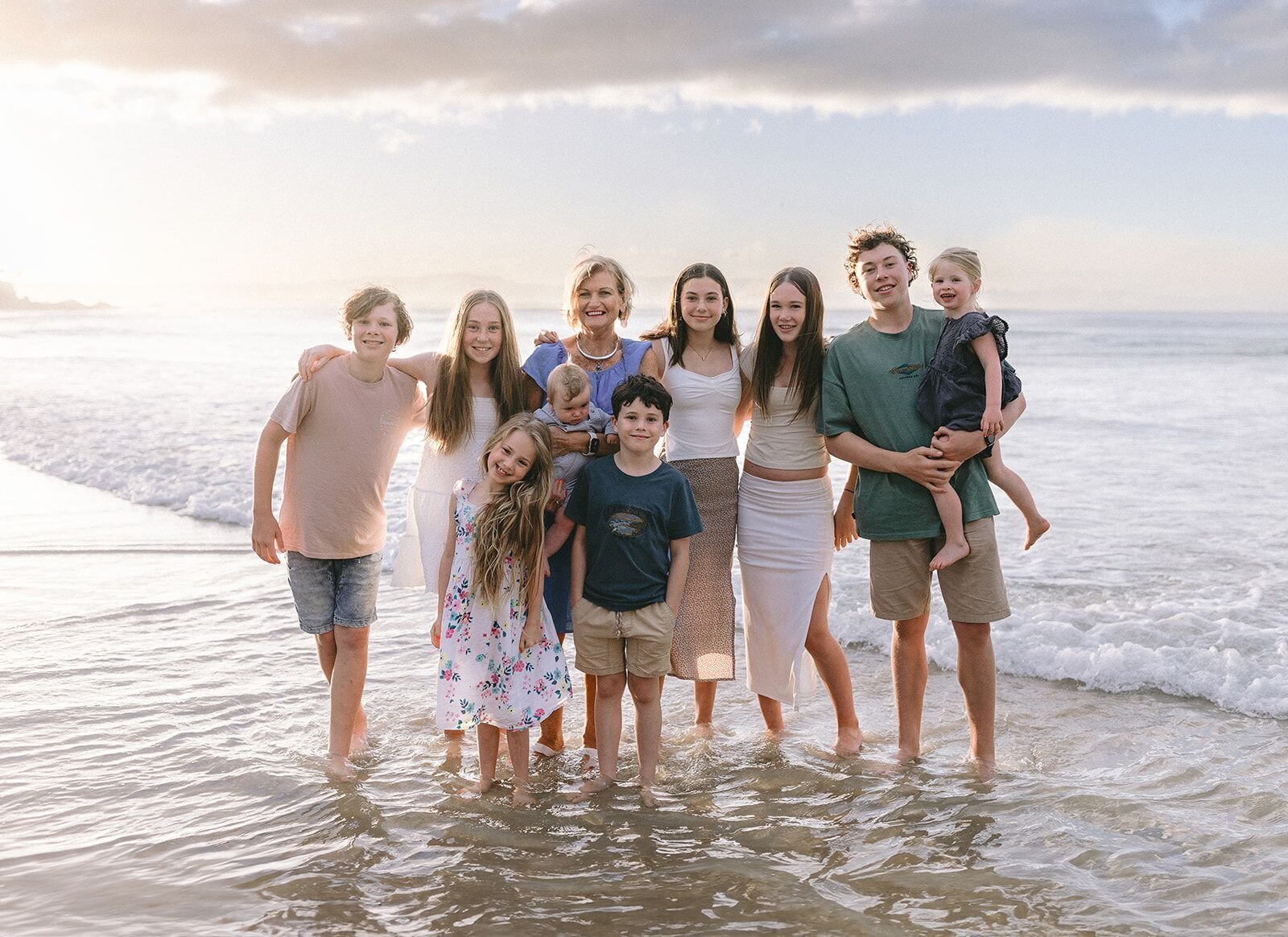 Large extended family standing together in the shallows at Wategos Beach at sunset, Byron Bay