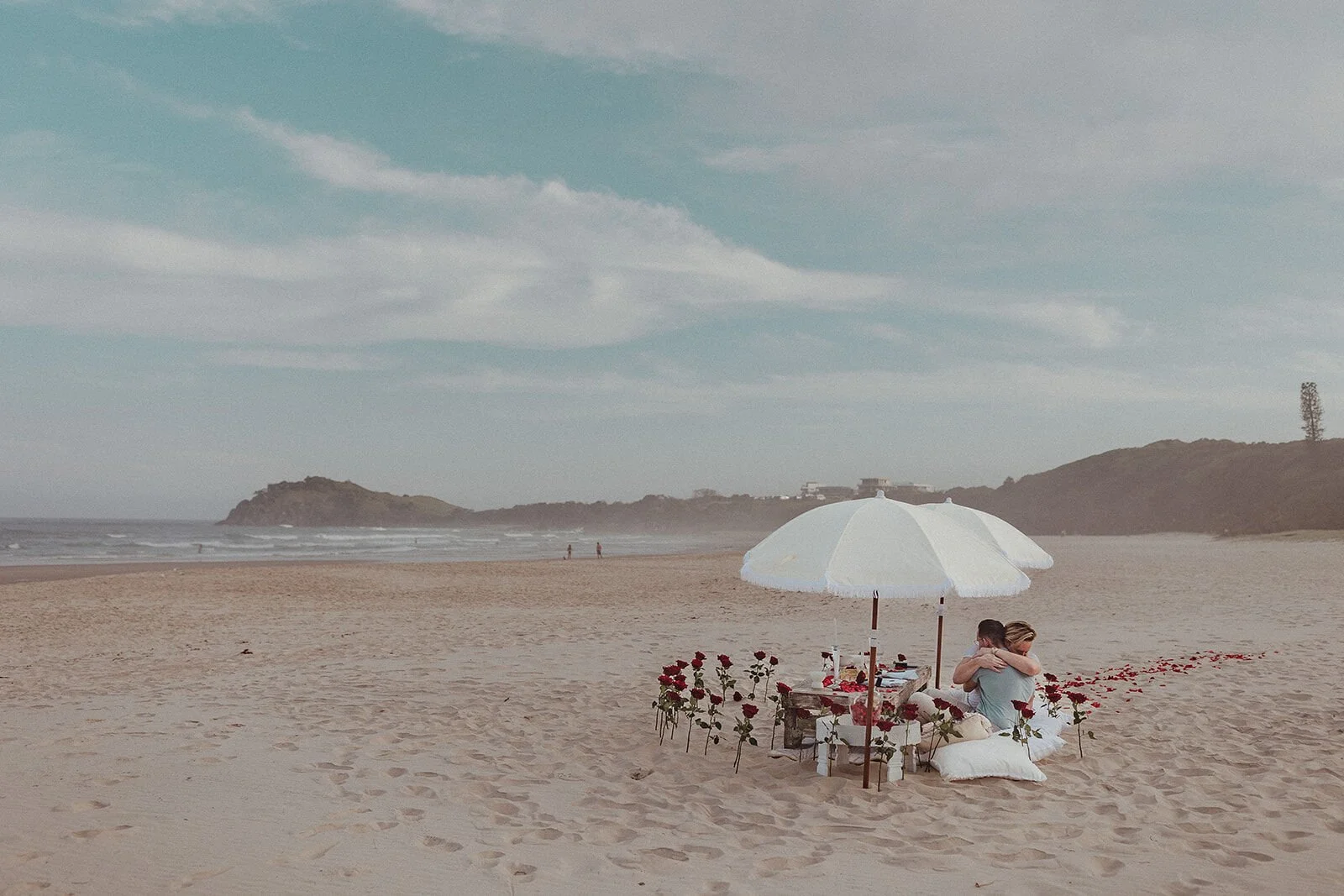 Wide beach view of the couple at their picnic with the headland behind, Byron and Luke's marriage proposal at Cabarita Beach, Northern Rivers