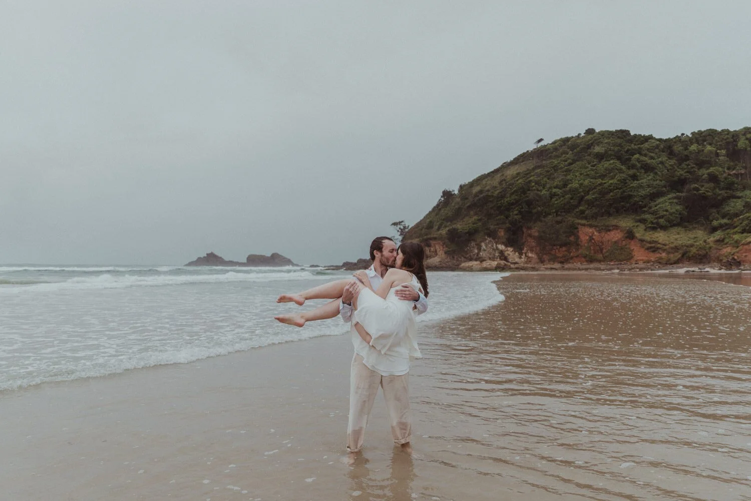 Groom carrying the bride along the shoreline, Yoanne and Elisa's rainy elopement at Broken Head, Byron Bay