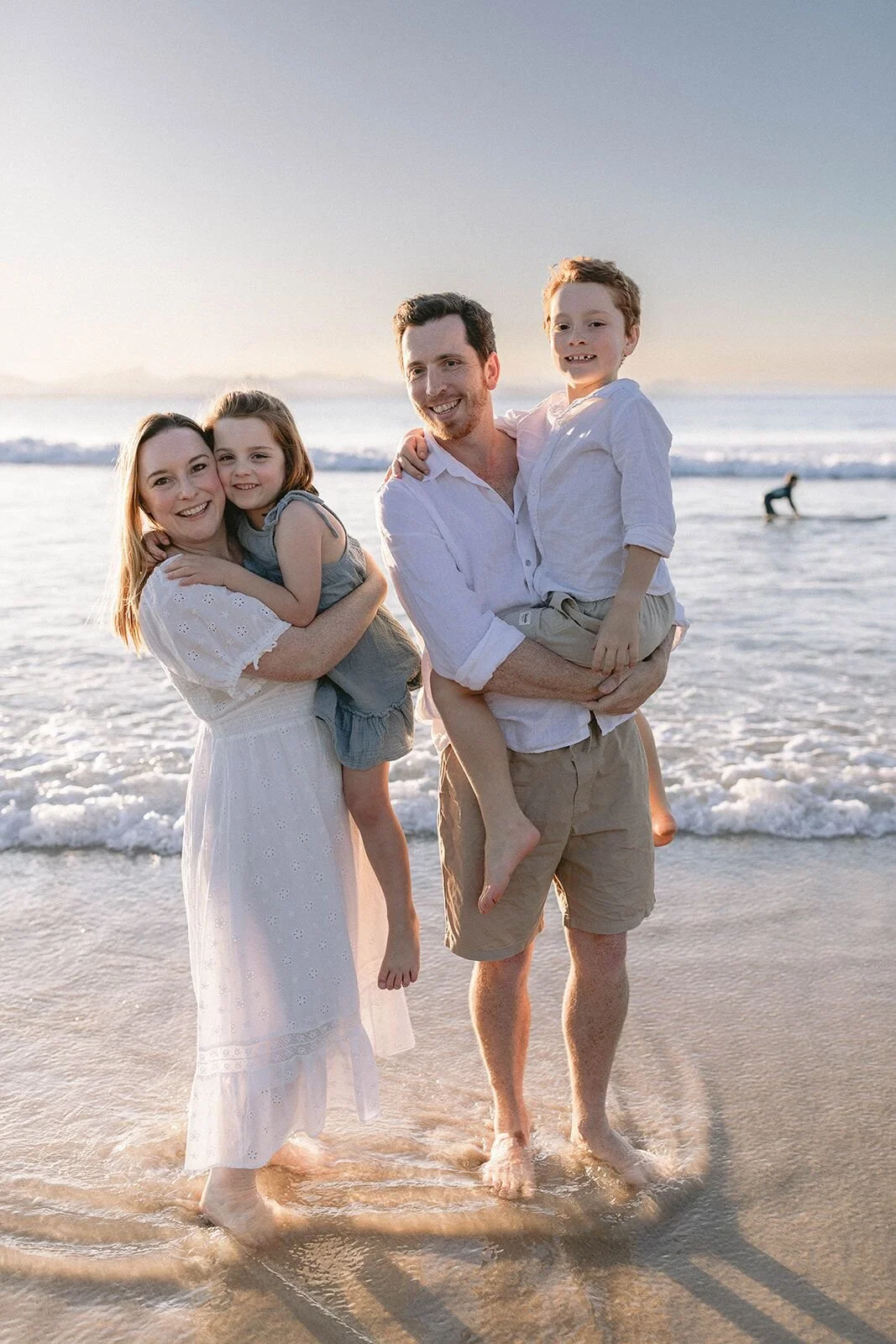 Family wading in the shallows at sunset, mum and dad each carrying one of their children