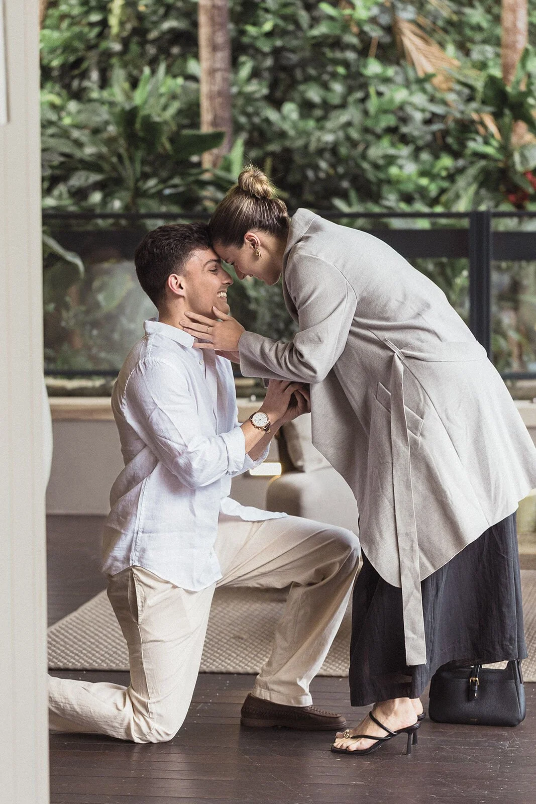 Woman leaning in to hold her partner's face as he kneels with the ring, Ben and Chloe's marriage proposal in Byron Bay