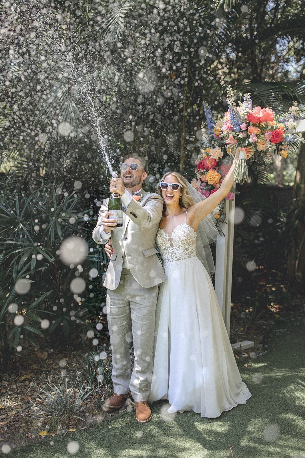 Couple popping champagne in sunglasses, Eliza and Greg's elopement at Broken Head, Byron Bay