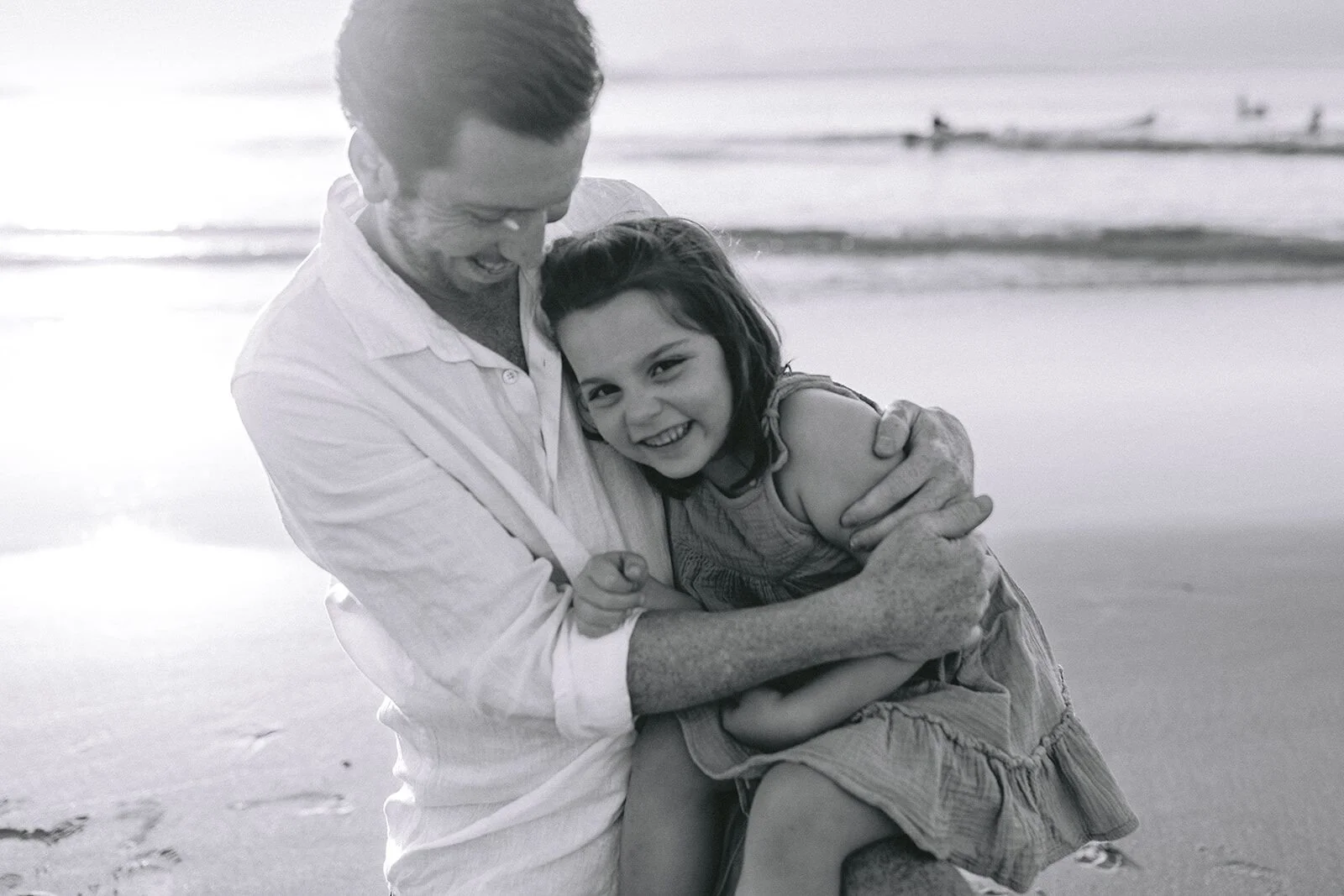Black and white photo of dad holding his daughter close as she smiles at the camera