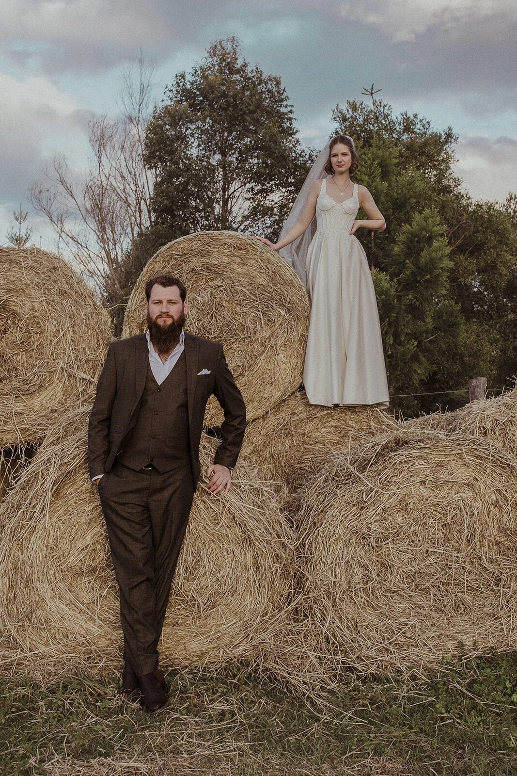 Groom leaning on hay bales with the bride standing above, Sam and Tom's elopement at Highfield Farm, Northern Rivers