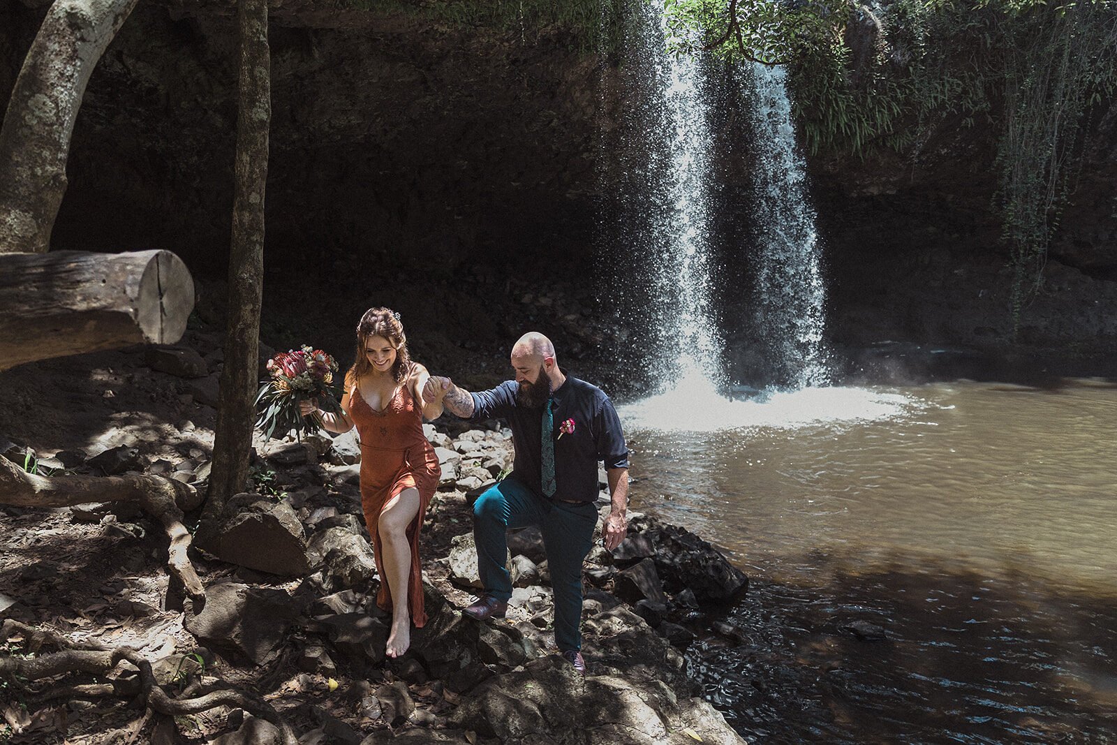 Couple stepping over rocks beside Killen Falls, Sara and Graeme's elopement, Northern Rivers