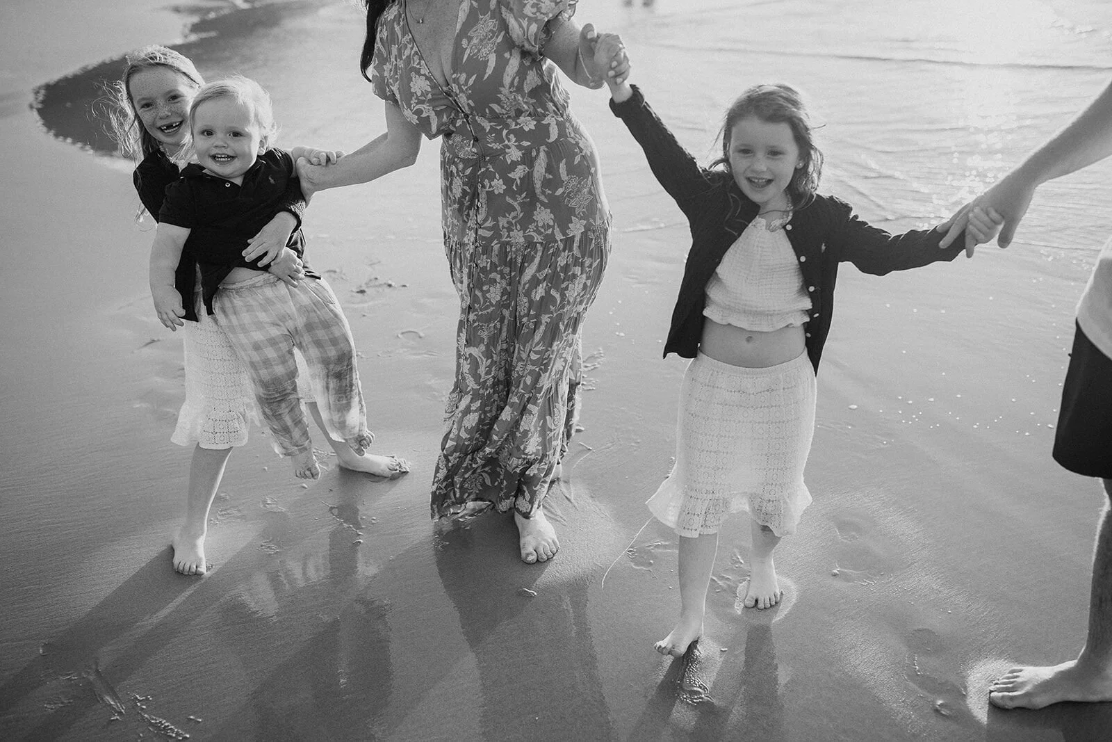 Black and white photo of the kids running hand in hand with mum on the beach