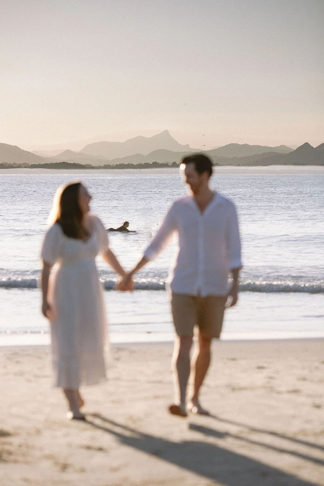 Mum and dad holding hands and walking along the beach at dusk, mountains behind