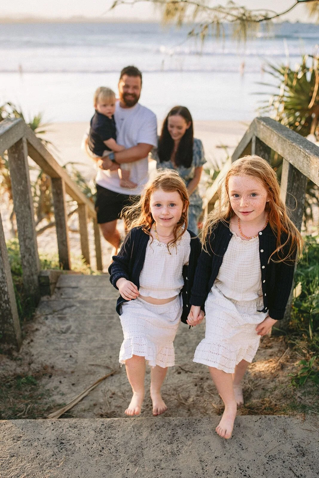 Two sisters walking up the beach steps toward the camera with their parents and toddler brother behind