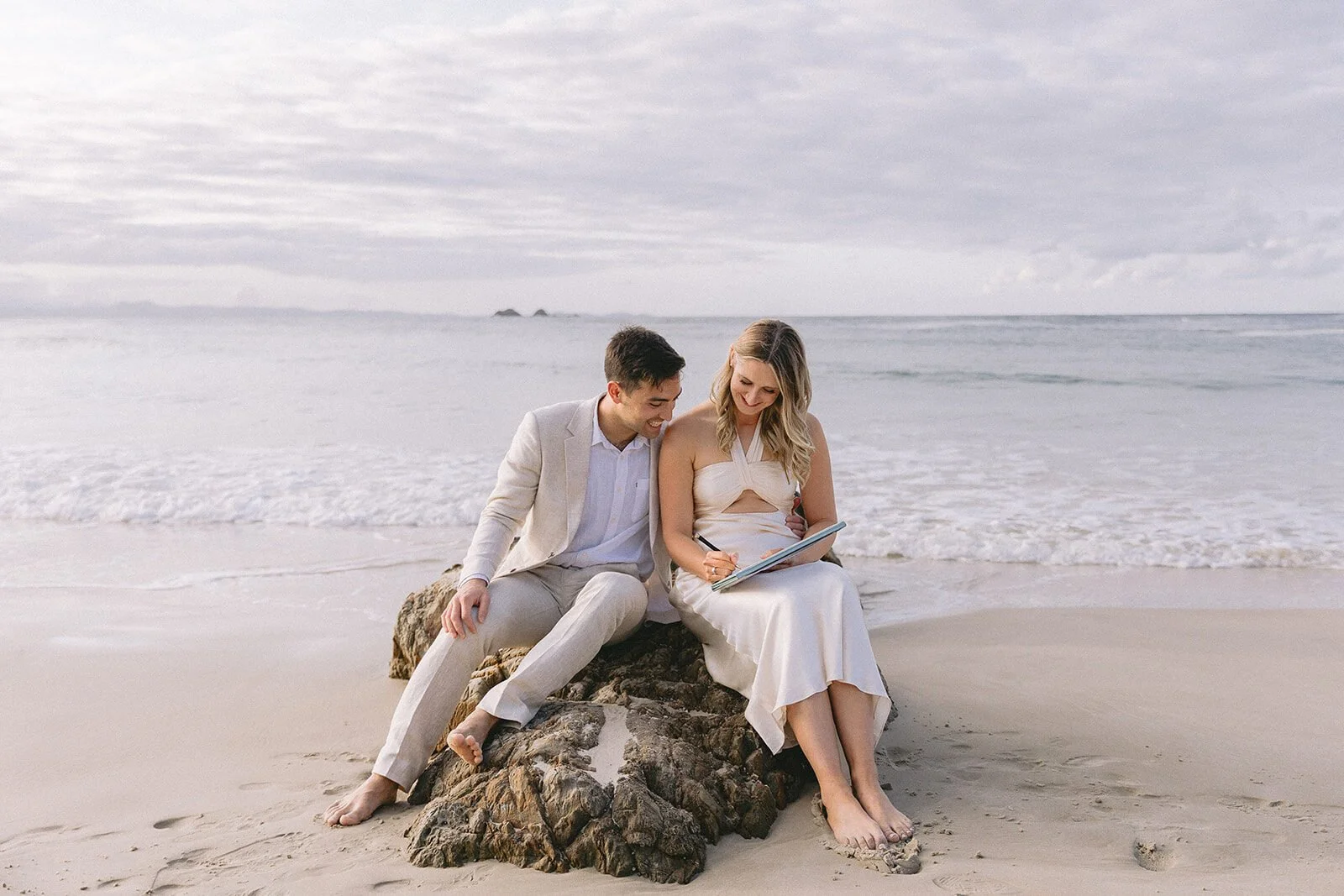 Couple sitting on a rock signing their marriage papers, Abby and James' elopement at Little Wategos Beach, Byron Bay