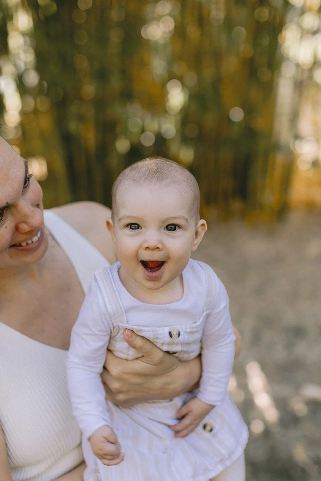 Baby girl with a huge open-mouthed smile held in mum's arms, warm golden light
