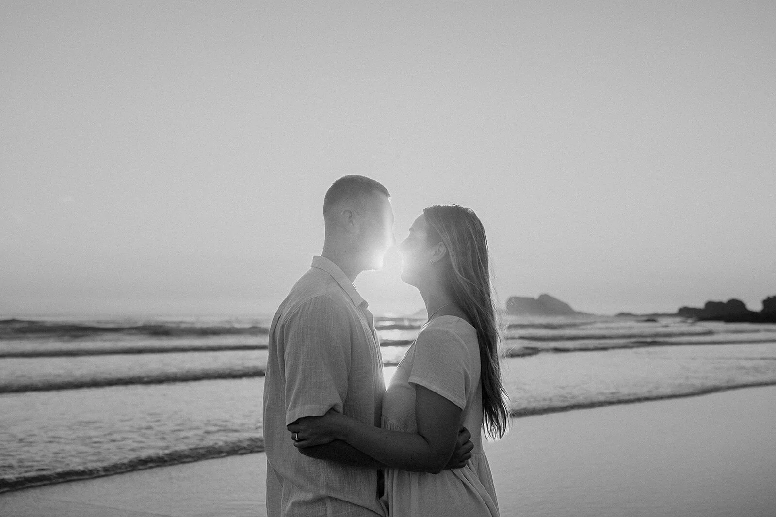 Black and white of the couple kissing with a sunburst between them, Charlie and Hannah's sunrise marriage proposal at Broken Head Beach, Byron Bay