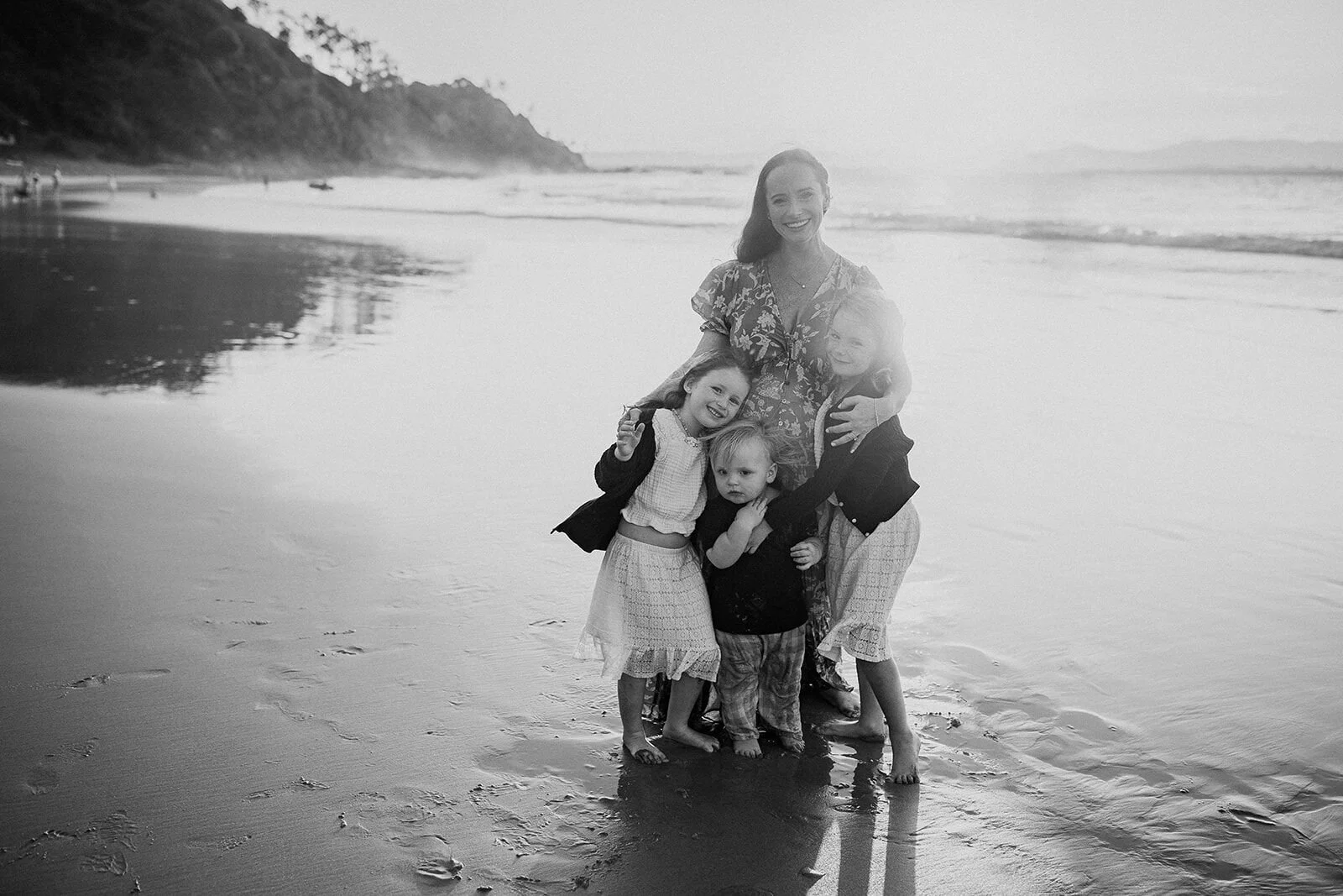 Black and white photo of mum with her three children on a wide, quiet beach
