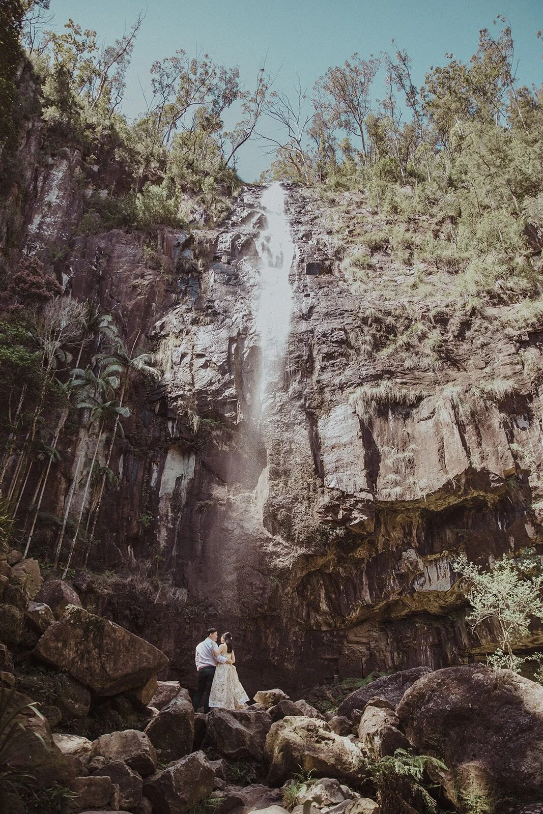 Couple kissing on the rocks below the waterfall cliff, Maggie and William's pre-wedding photos in Byron Bay