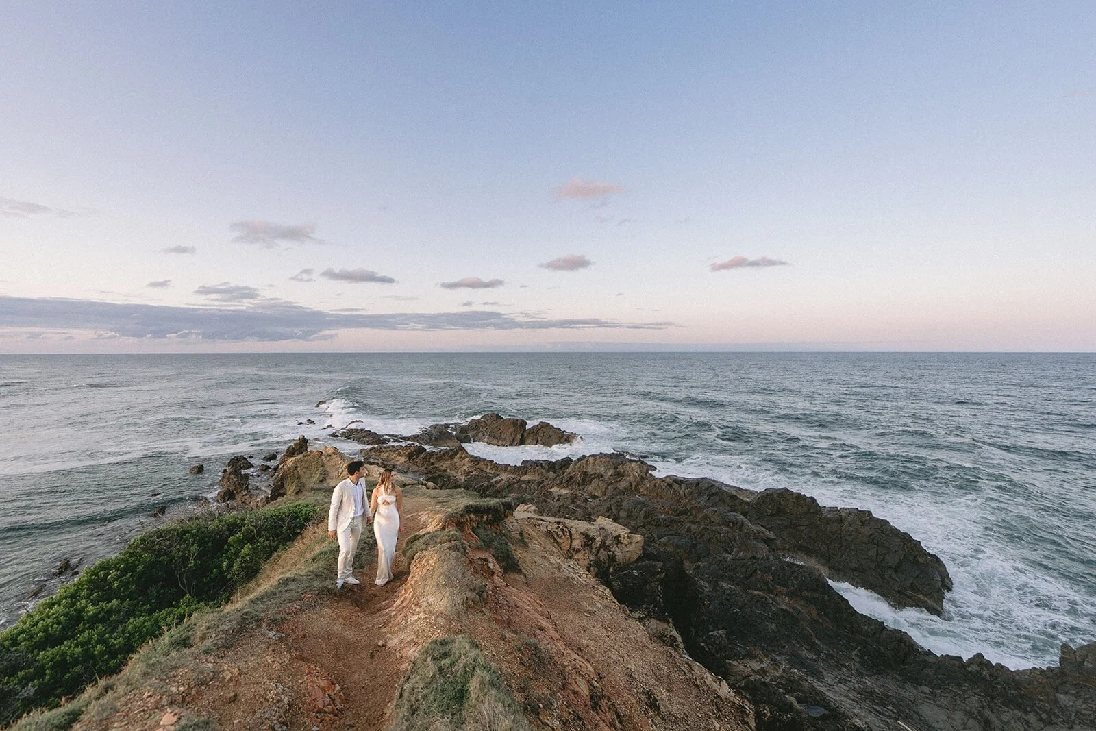 Couple walking the narrow headland path above the waves, Abby and James' elopement at Little Wategos Beach, Byron Bay
