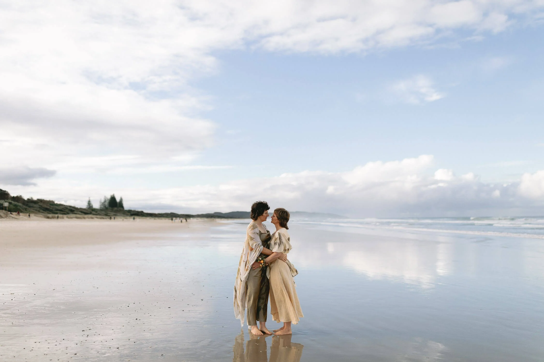 Two brides embracing on the wet sand at Seven Mile Beach, Lennox Head