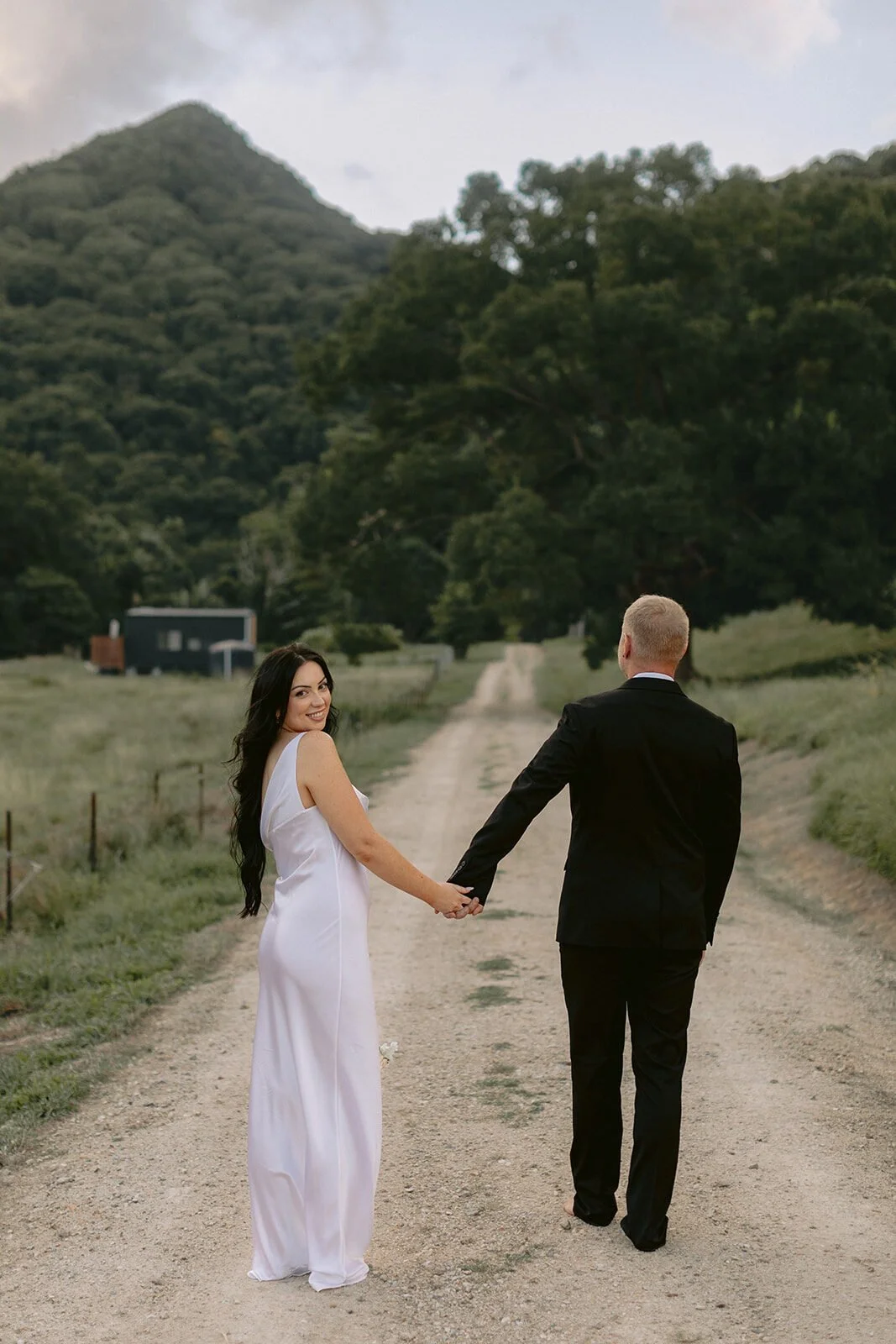 Couple walking hand in hand down a dirt road toward a tiny house, Kobi and Darren's elopement at Butterfly Lane, Byron Bay hinterland