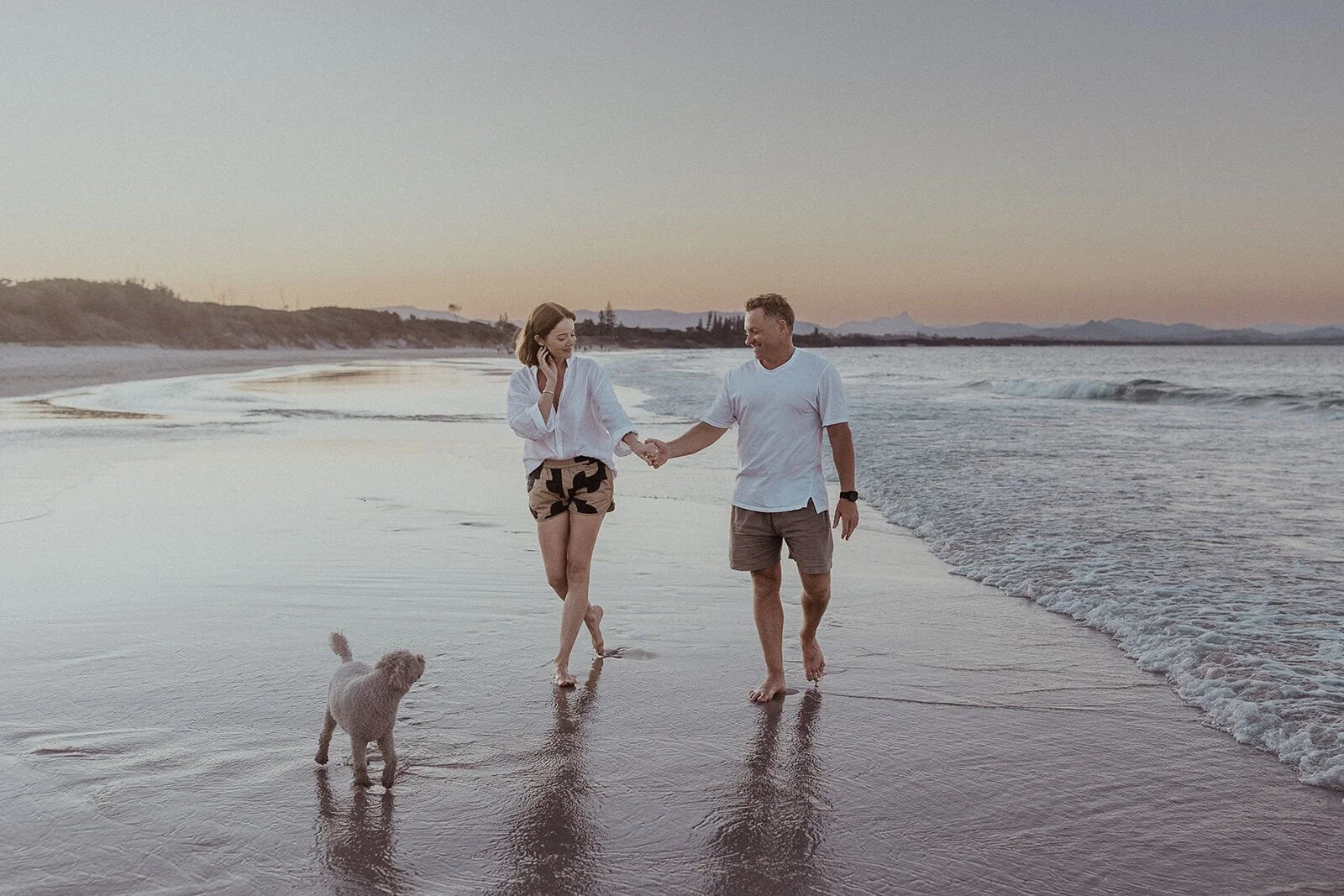 Couple walking hand in hand along the shoreline with their dog, Jamie and Jessica's beach marriage proposal at Belongil Beach, Byron Bay