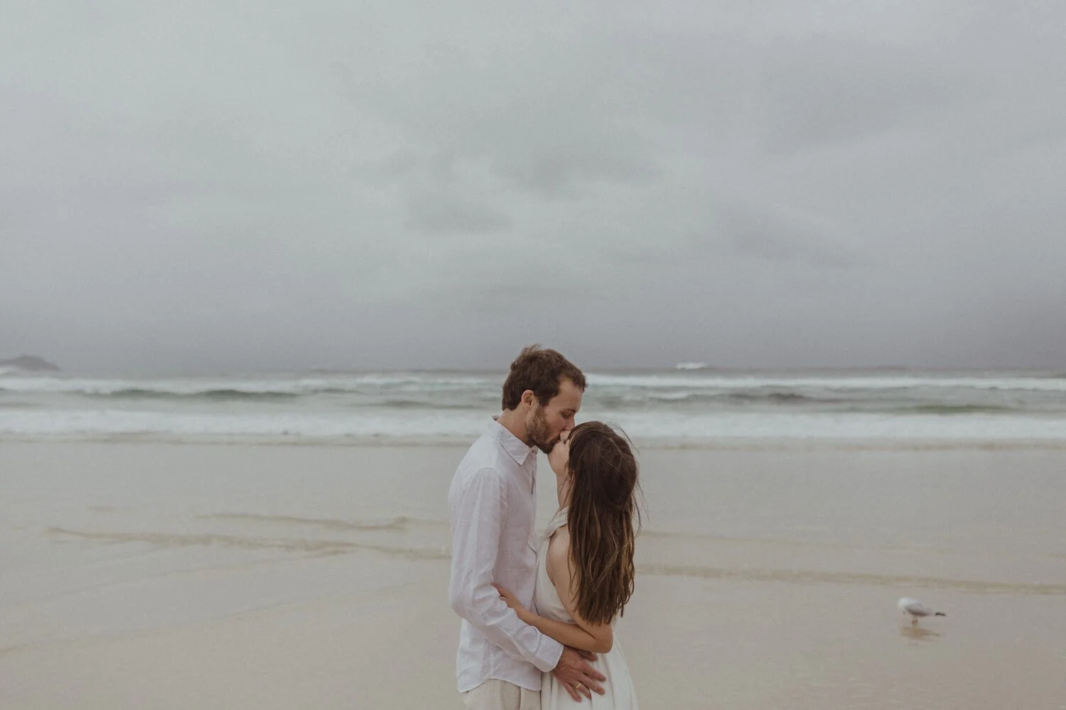 Couple kissing on the beach under a moody sky, Yoanne and Elisa's rainy elopement at Broken Head, Byron Bay