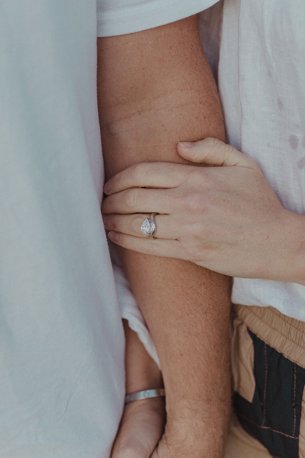 Close up of her engagement ring resting on his arm, Jamie and Jessica's beach marriage proposal at Belongil Beach, Byron Bay