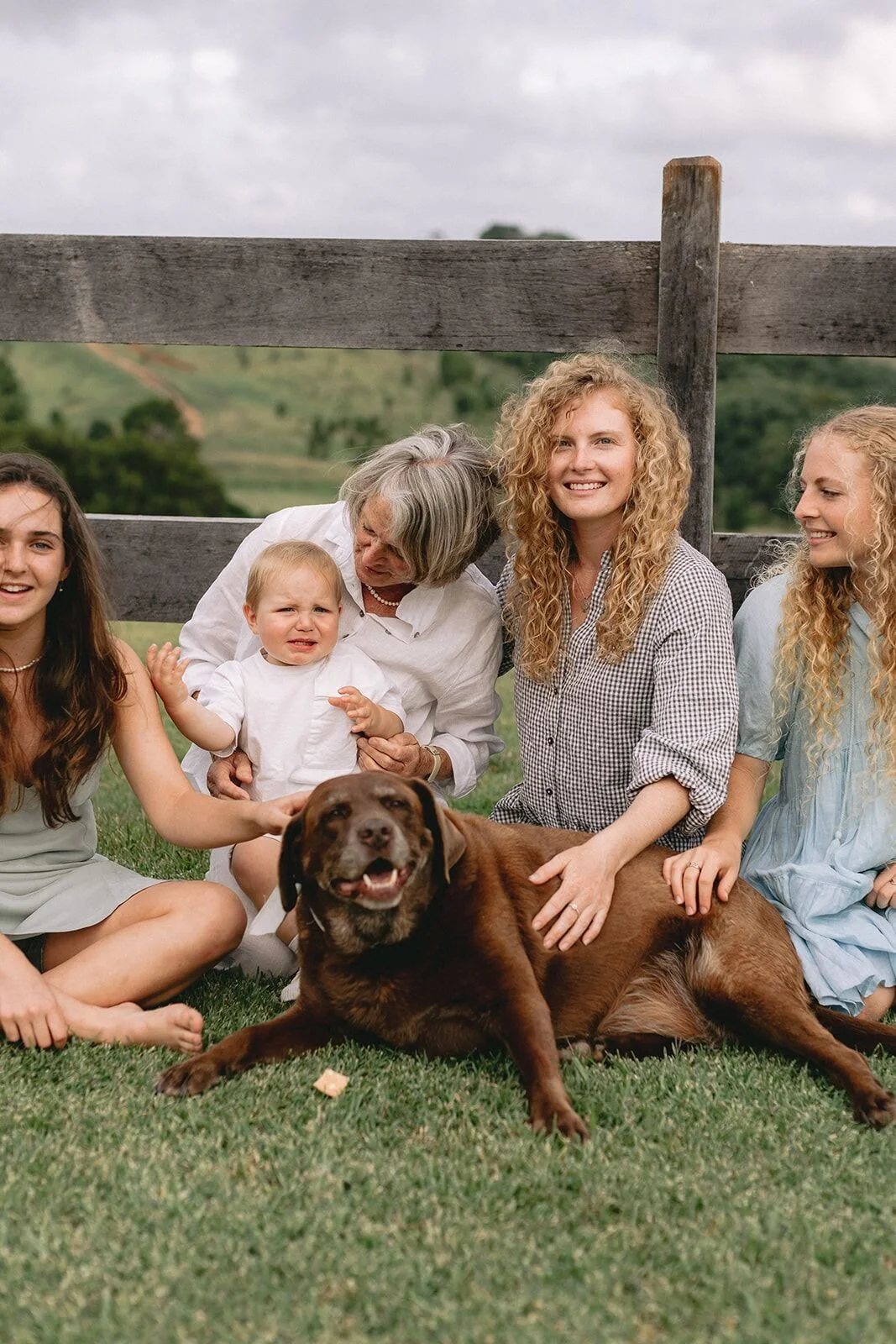 Grandmother holding her grandson with the family dog and granddaughters beside her on the grass